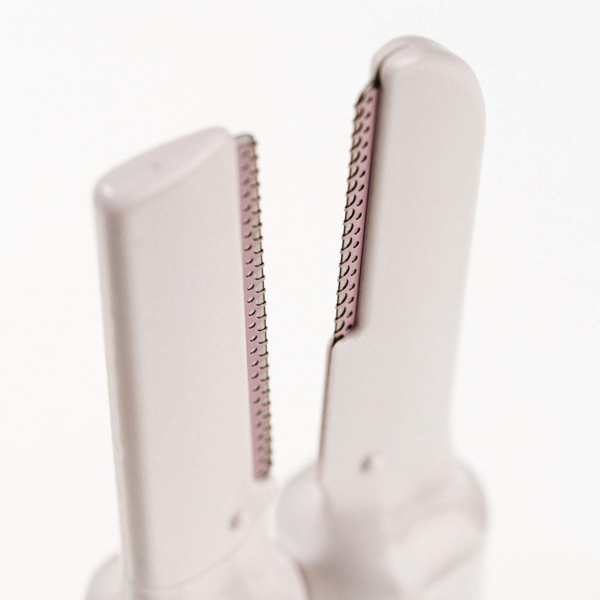 Close-up of two white dermaplaning blade heads with fine pink-guarded edges