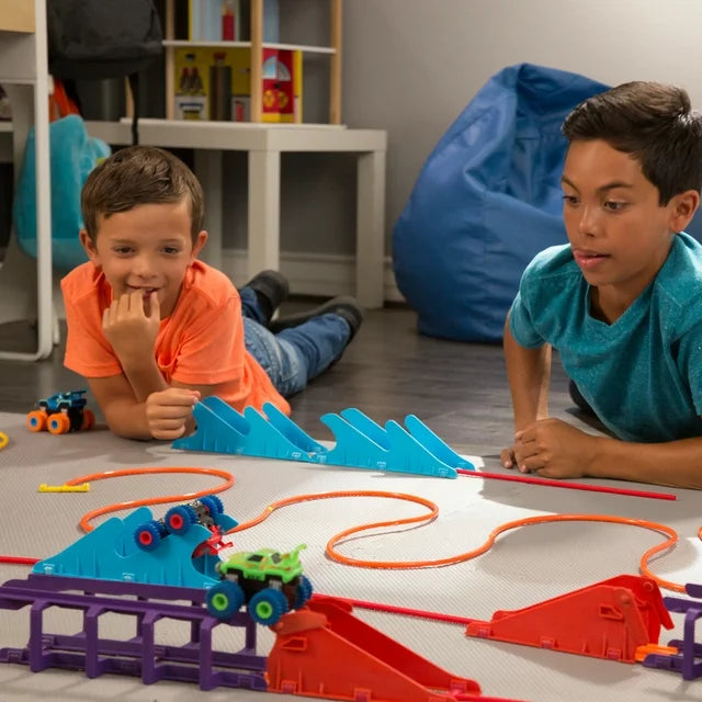 Two boys watching trucks run on an orange rope track with blue ramps