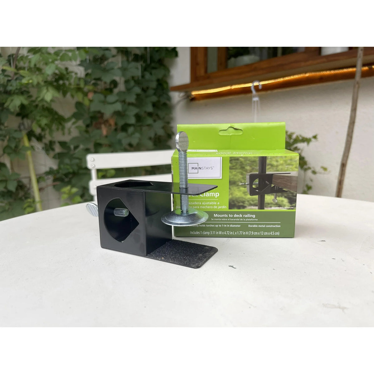 Black metal deck clamp with silver thumbscrews in front of its green box on a patio table