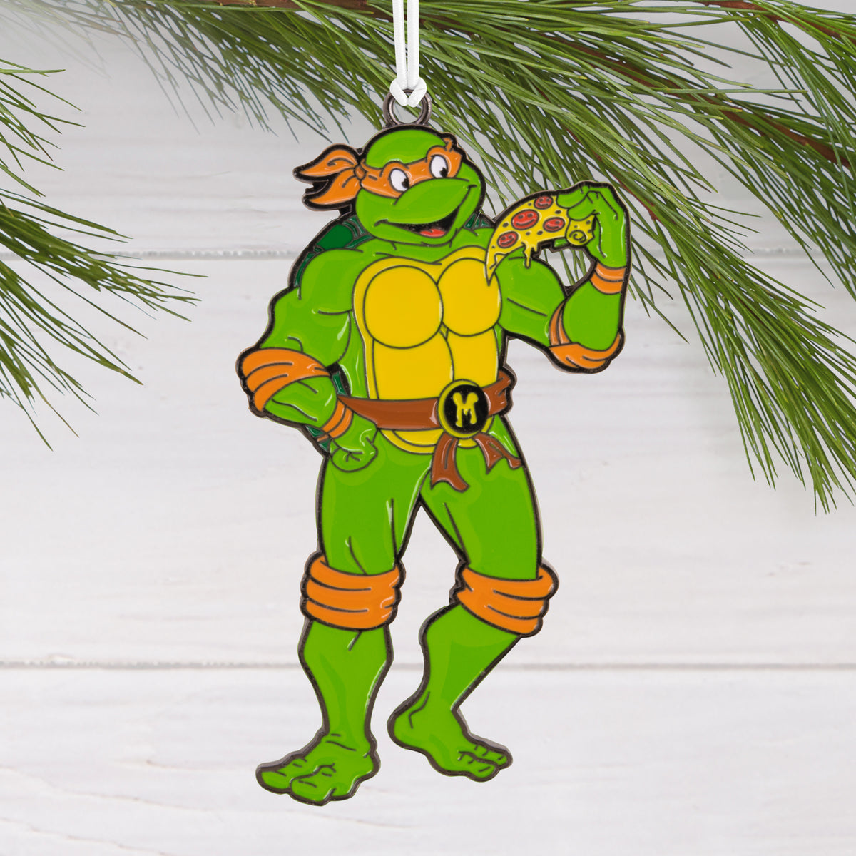 Enamel pizza-eating turtle ornament hanging from a pine branch