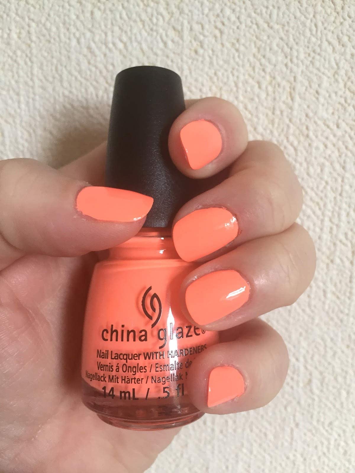 Hand with neon coral painted nails holding the coral nail polish bottle