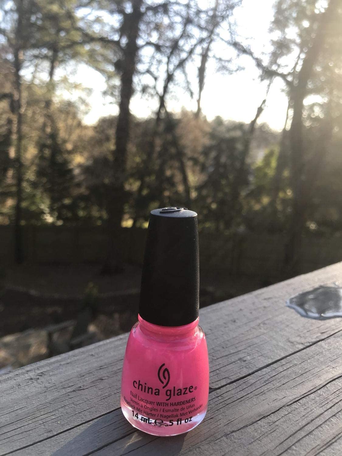 Hot pink polish bottle on a wooden deck rail with trees behind