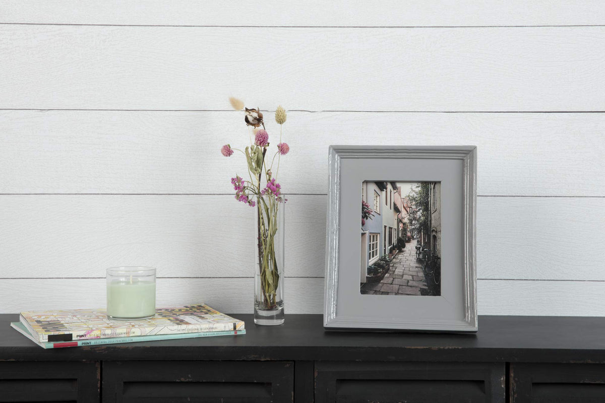 Glossy grey picture frame with a street photo beside dried flowers and a candle
