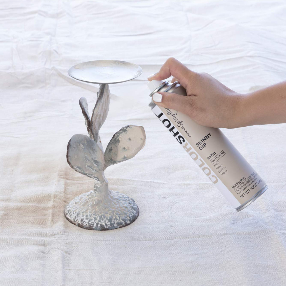 Hand spraying beige paint onto a grey metal cactus candle holder