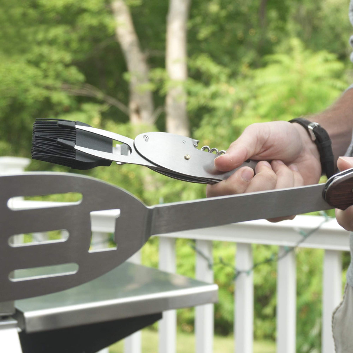 Hands separating the grill multi-tool by a barbecue, showing the brush and spatula halves