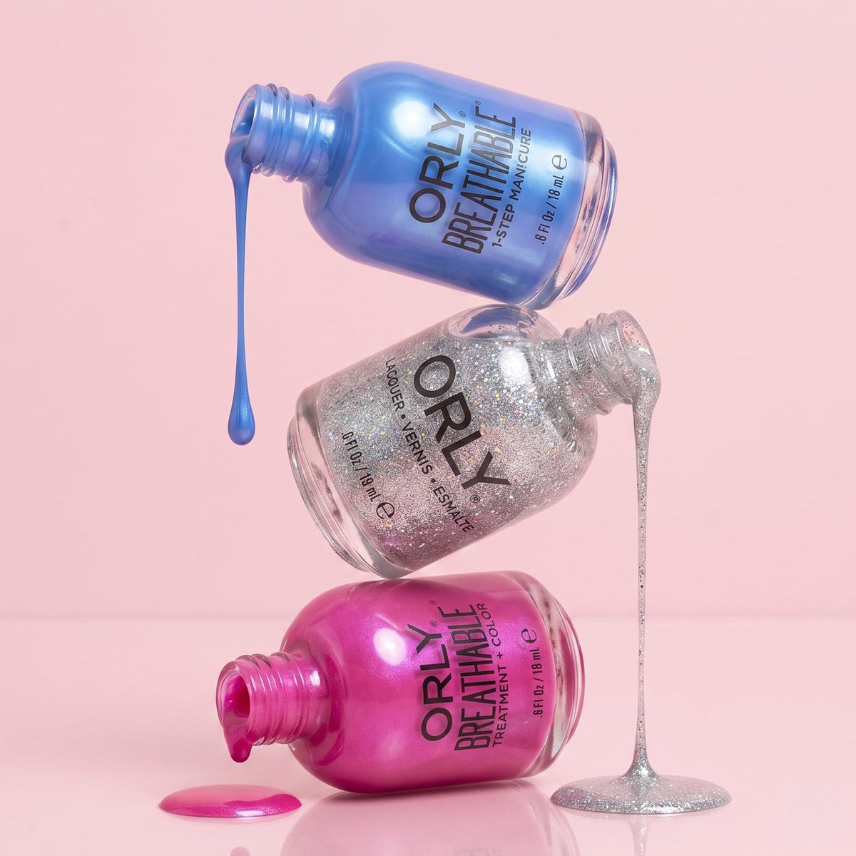 Blue, silver glitter and pink Orly polish bottles stacked and dripping on a pink background