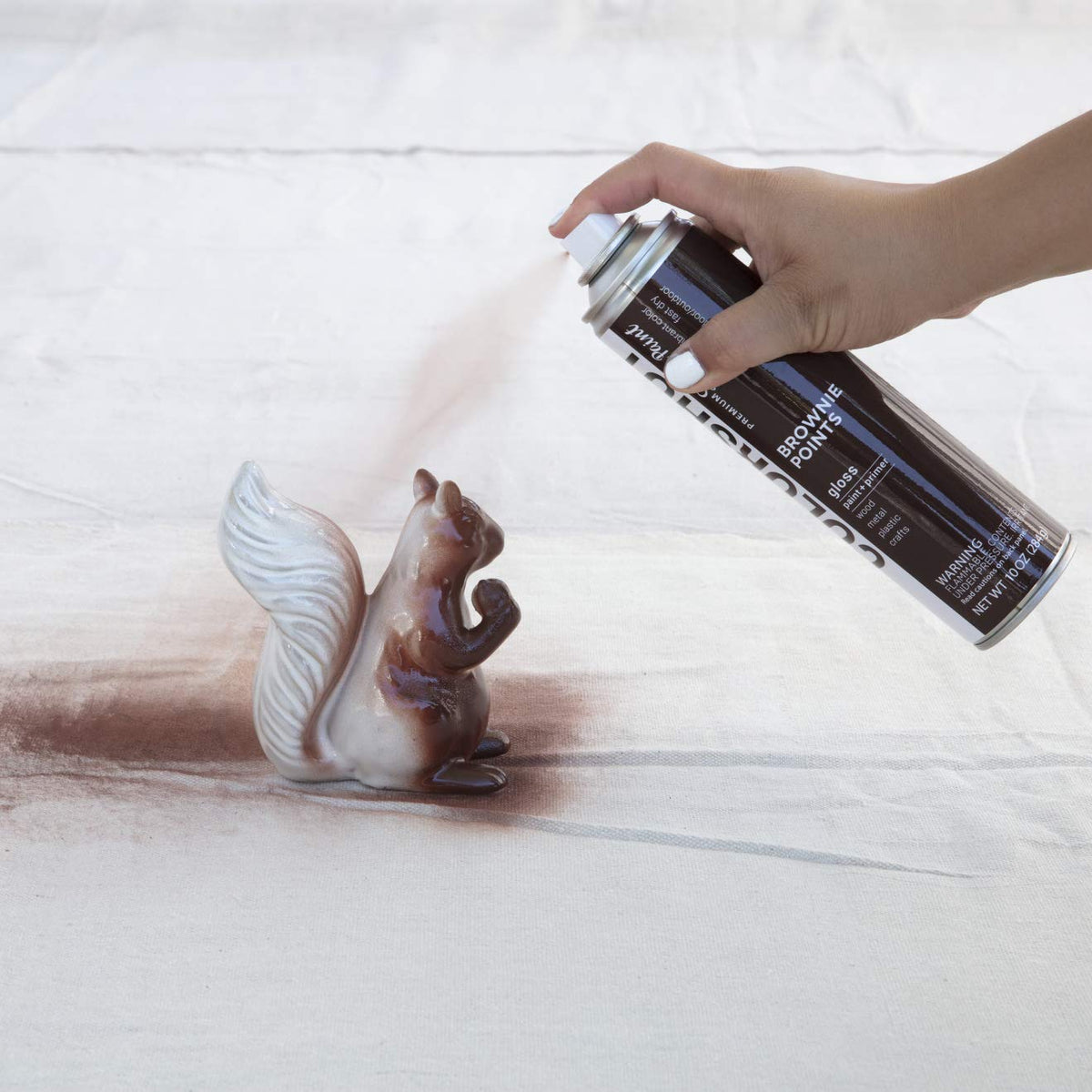 Hand spraying dark brown paint onto a white ceramic squirrel