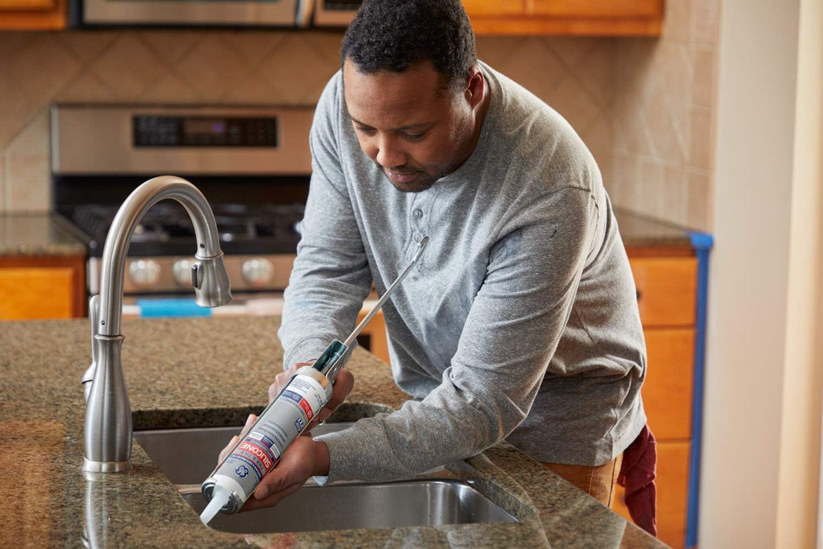 Man running a bead of silicone around a kitchen sink with a caulk gun
