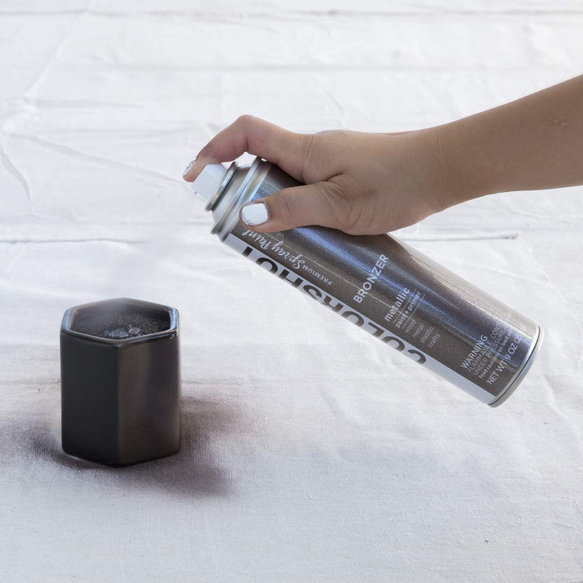 Hand spraying metallic bronze paint onto a hexagonal pot