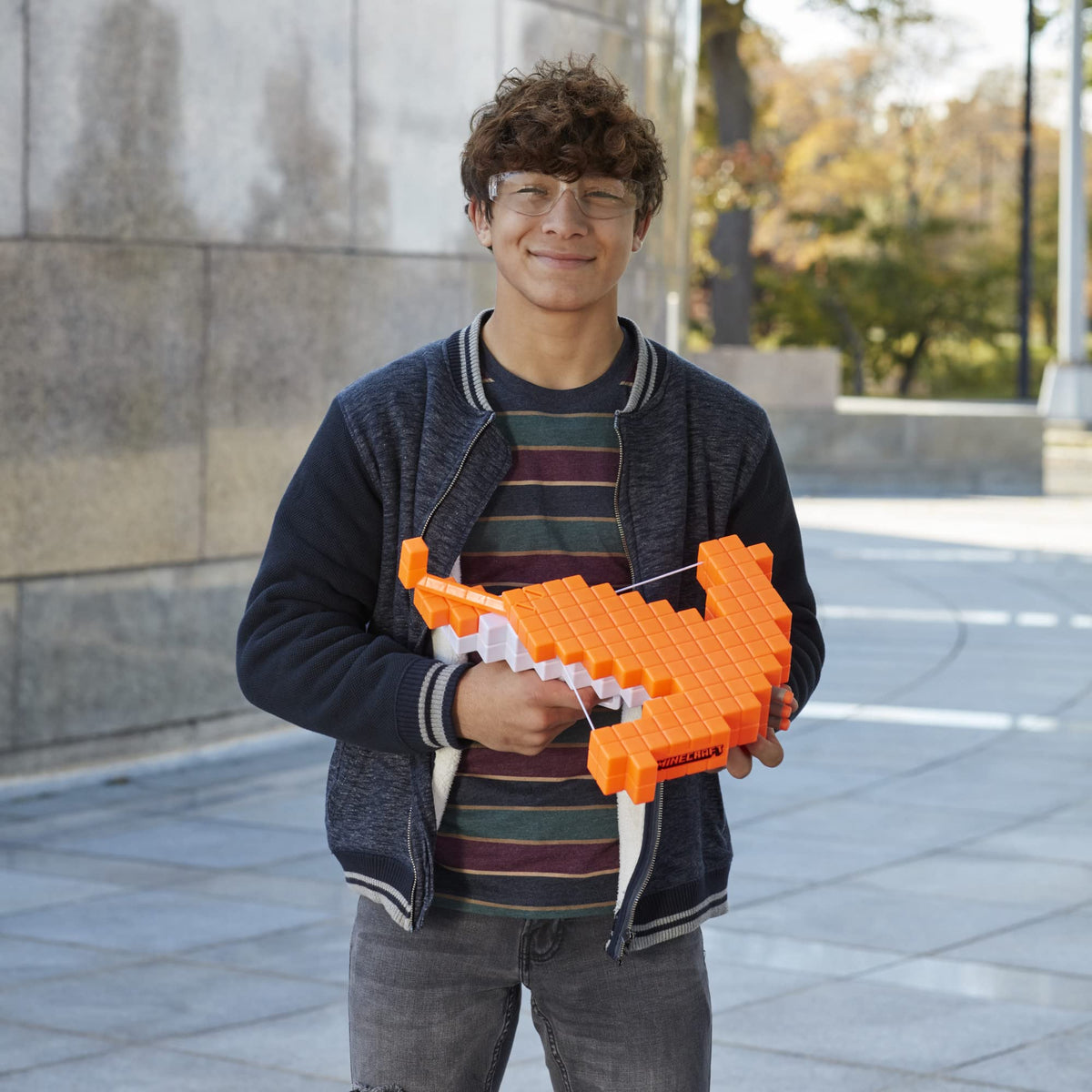 Teen in safety glasses holding the orange crossbow in front of a stone wall