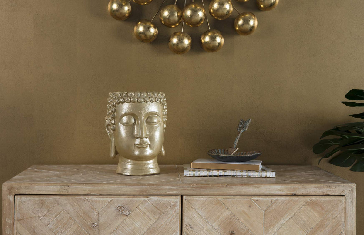 Metallic gold head-shaped planter on a wooden sideboard below gold wall decor