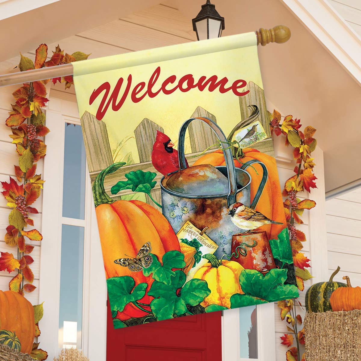 Welcome flag with cardinal, sparrow and pumpkins on a porch by a red door