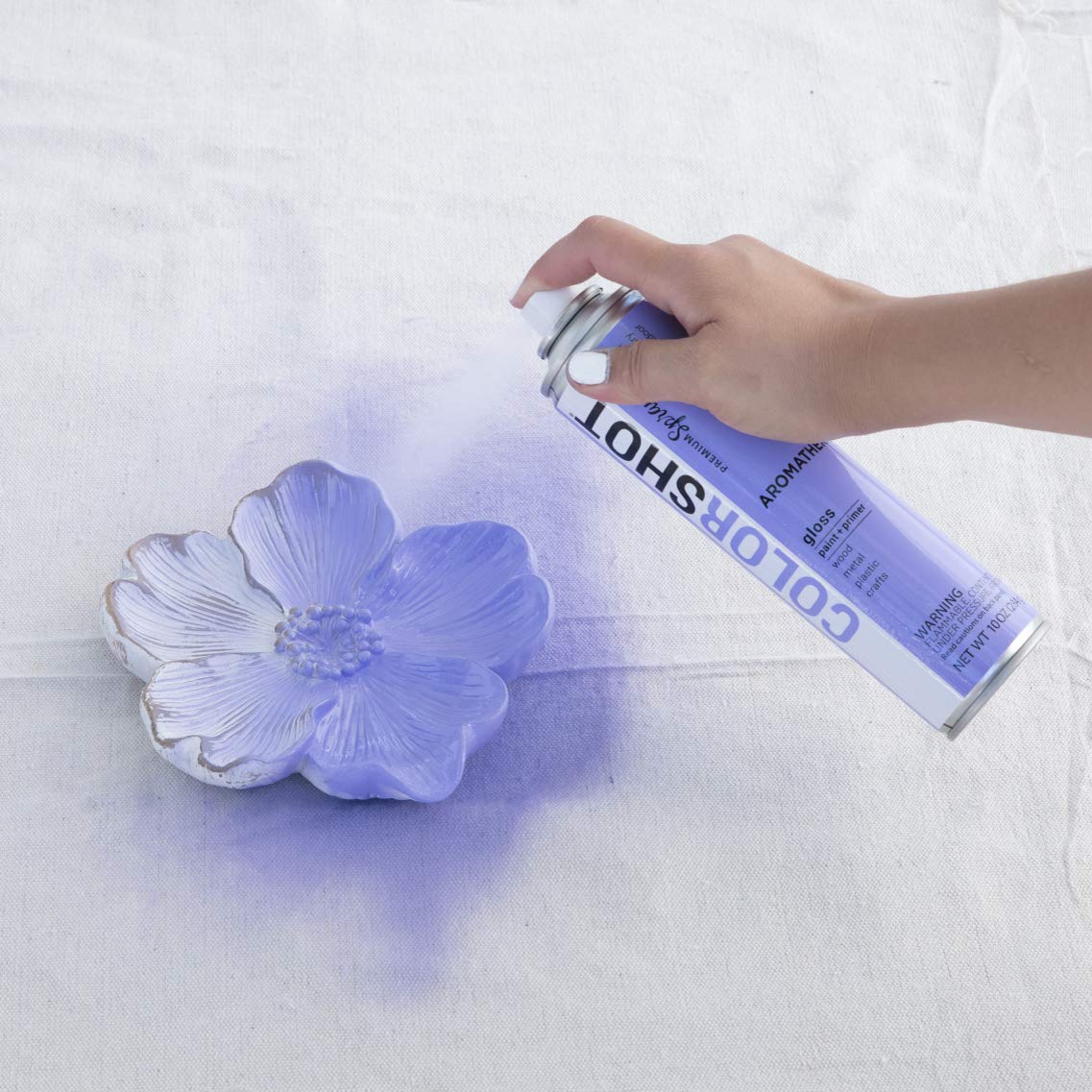 Hand spraying lavender paint onto a white flower-shaped dish