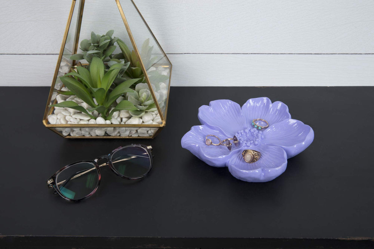 Glossy lavender flower-shaped ring dish beside a glass terrarium and glasses