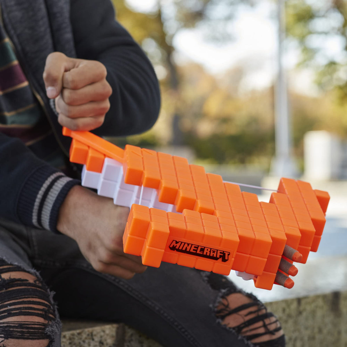 Teen pulling back the priming handle on the orange crossbow while seated outdoors