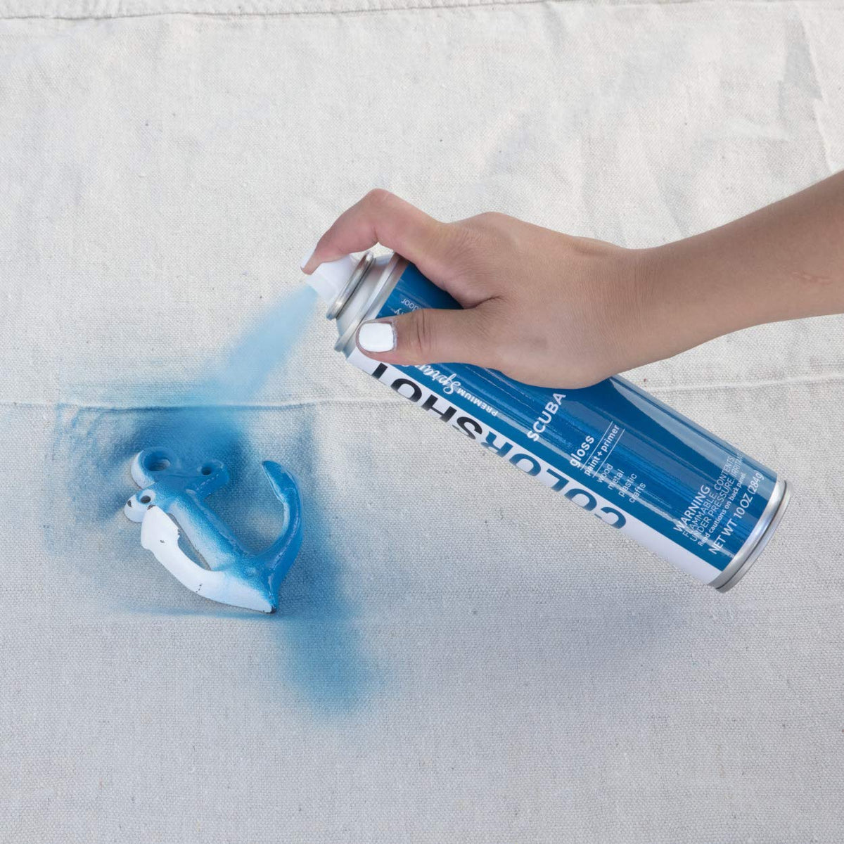Hand spraying marine blue paint onto a white metal anchor hook