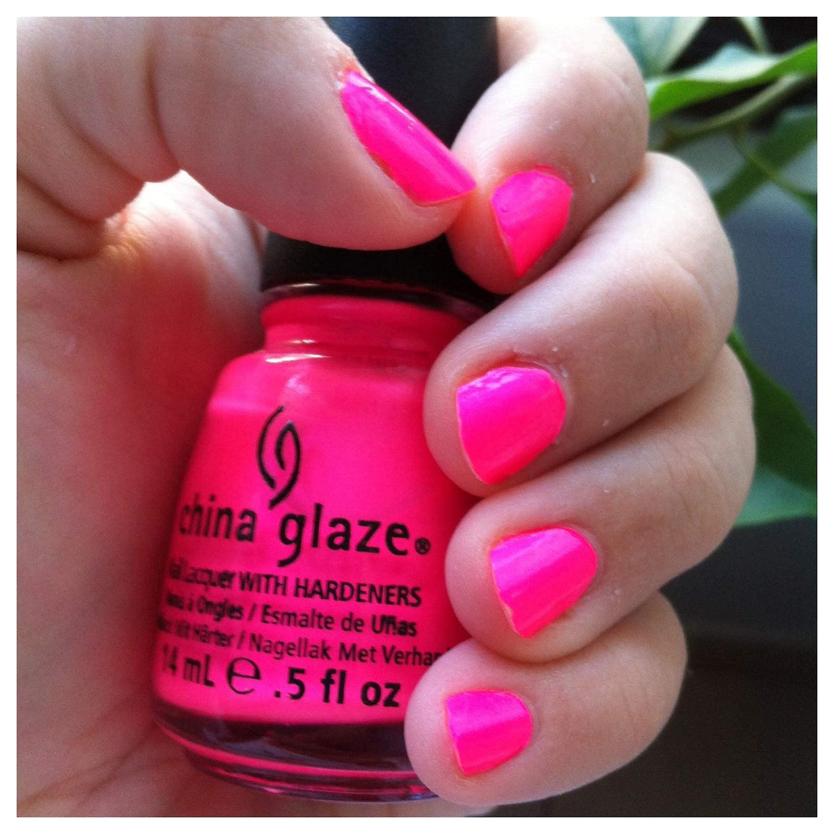 Hand with short neon pink nails holding the hot pink polish bottle
