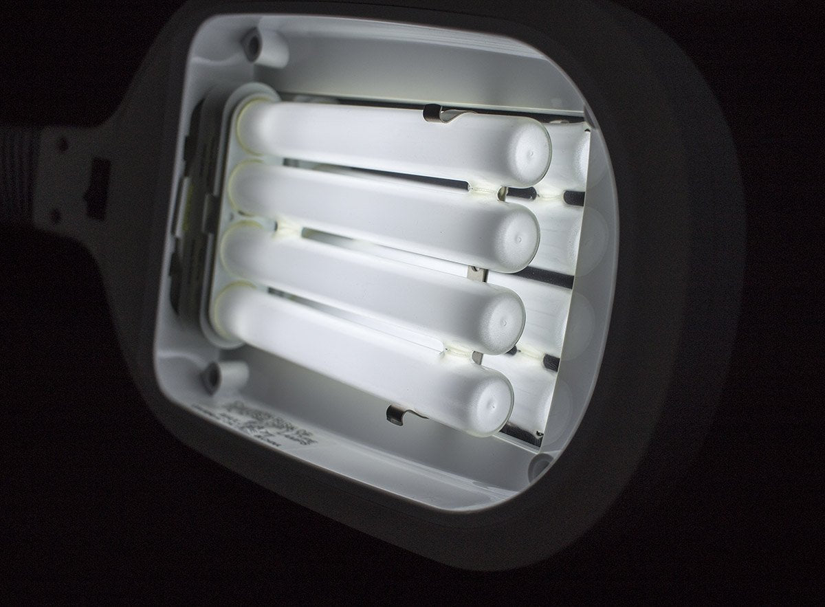 Four-tube fluorescent bulb glowing inside a lamp head in a dark room