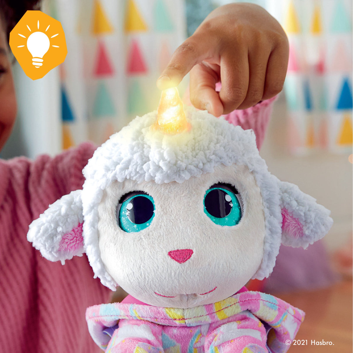 Close-up of a finger on the lit horn of the lamb plush with big teal eyes