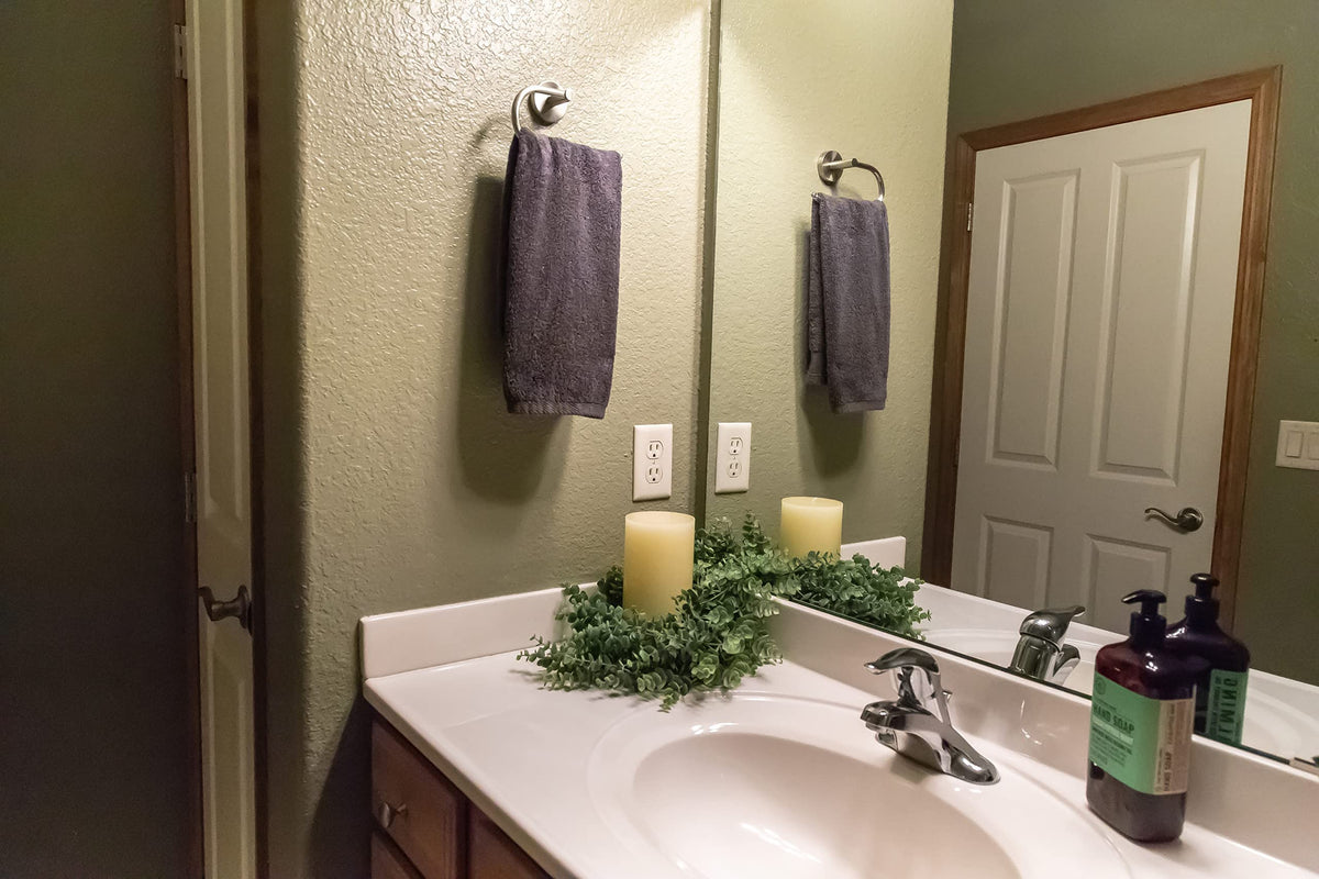 White marble vanity with side splash against a green wall, candle and greenery
