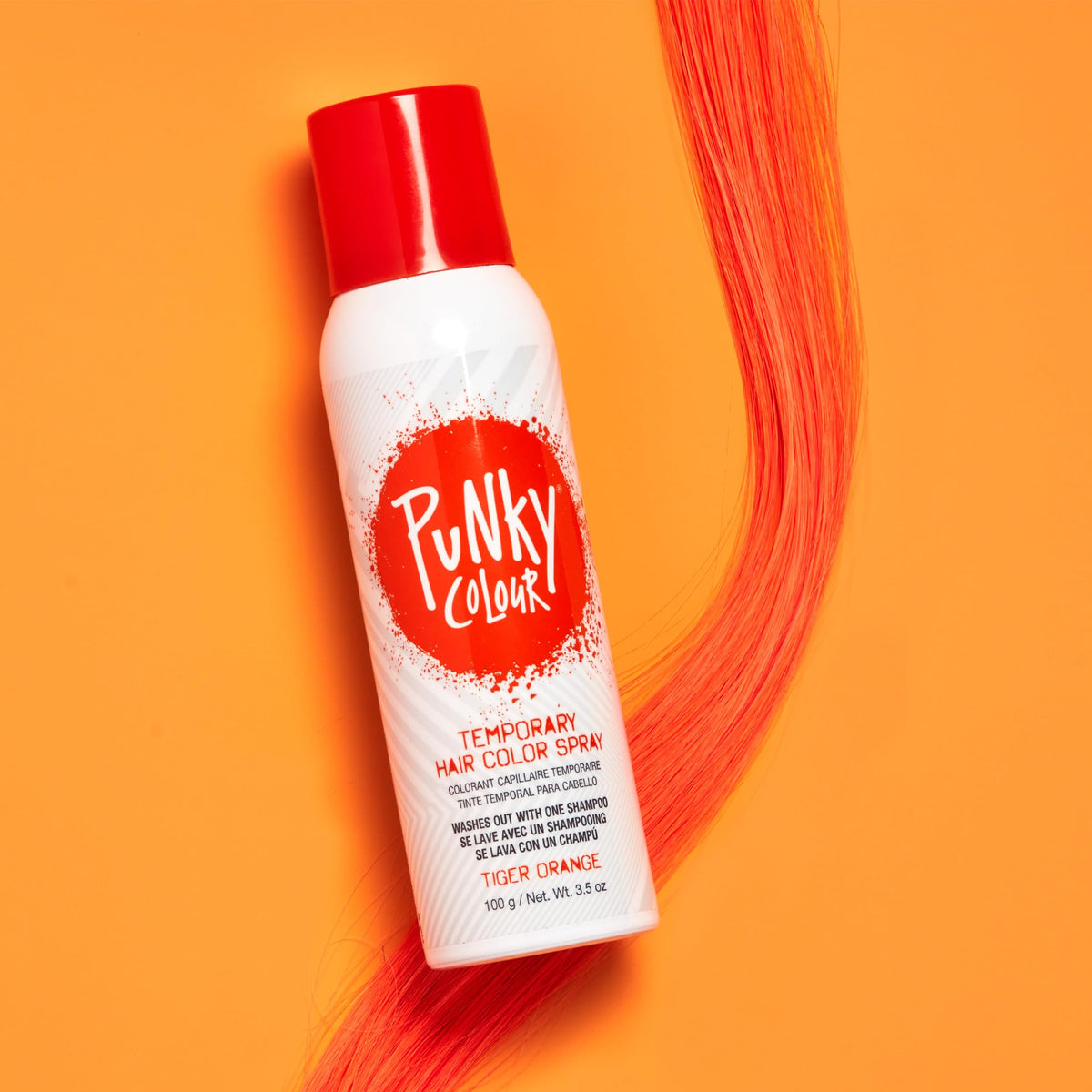 Tiger orange hair spray can lying beside a long orange hair strand on orange