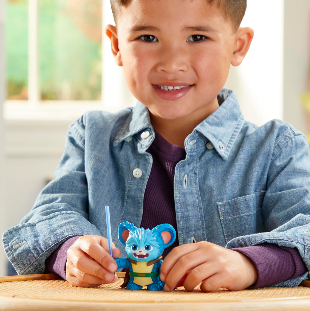 Smiling boy holding the blue creature figure and its lightsaber on a table
