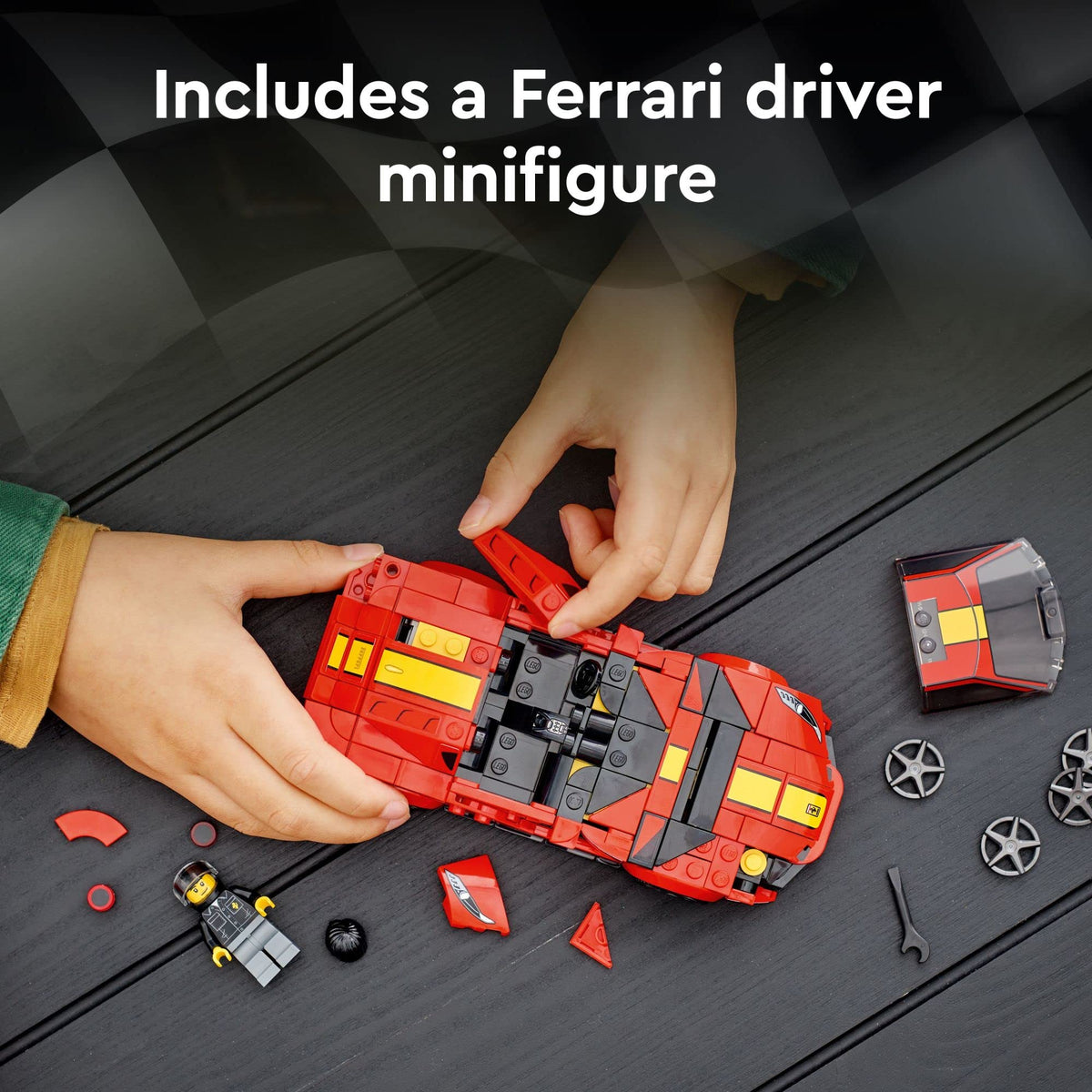 Child's hands building the red brick car with the minifigure, wheels and wrench nearby