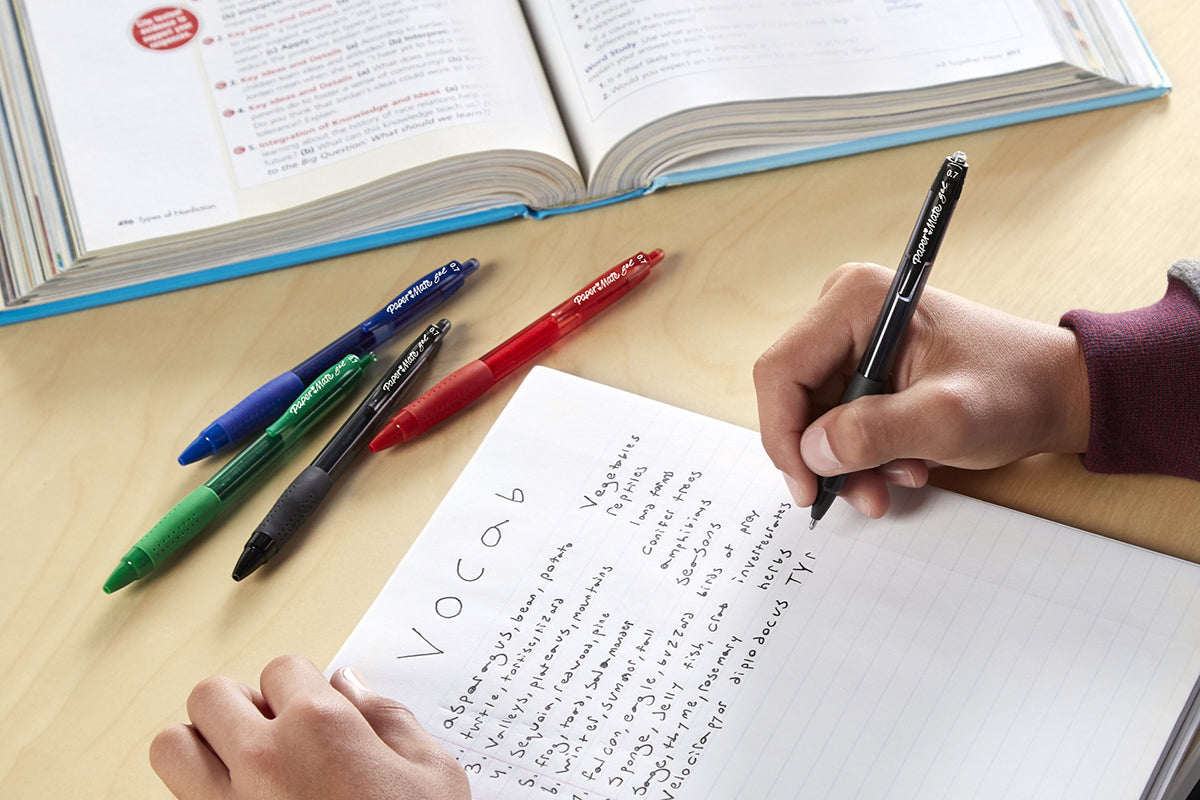 Student writing vocabulary notes with a black gel pen beside blue, green and red pens
