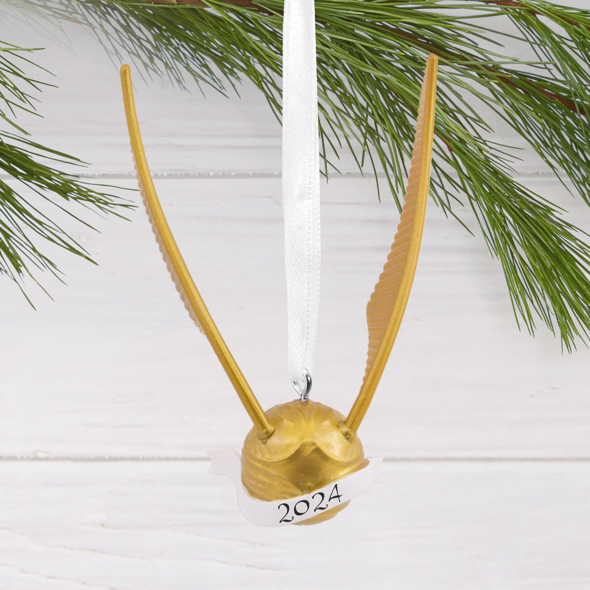 Gold winged ball ornament hanging from a pine branch