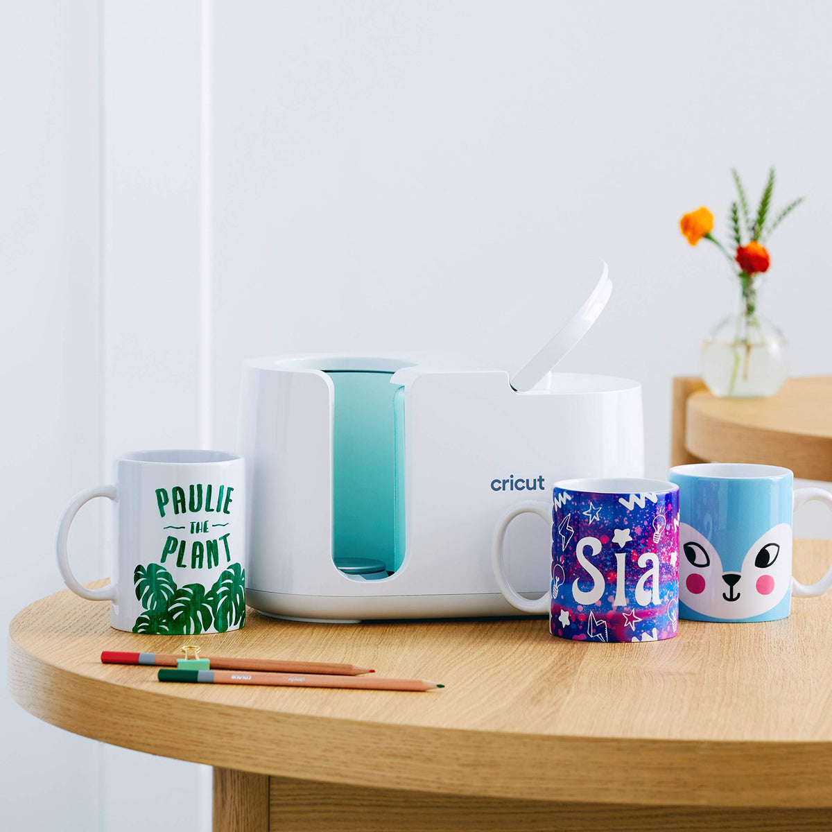 Cricut Mug Press on a wooden table with three personalized mugs it made