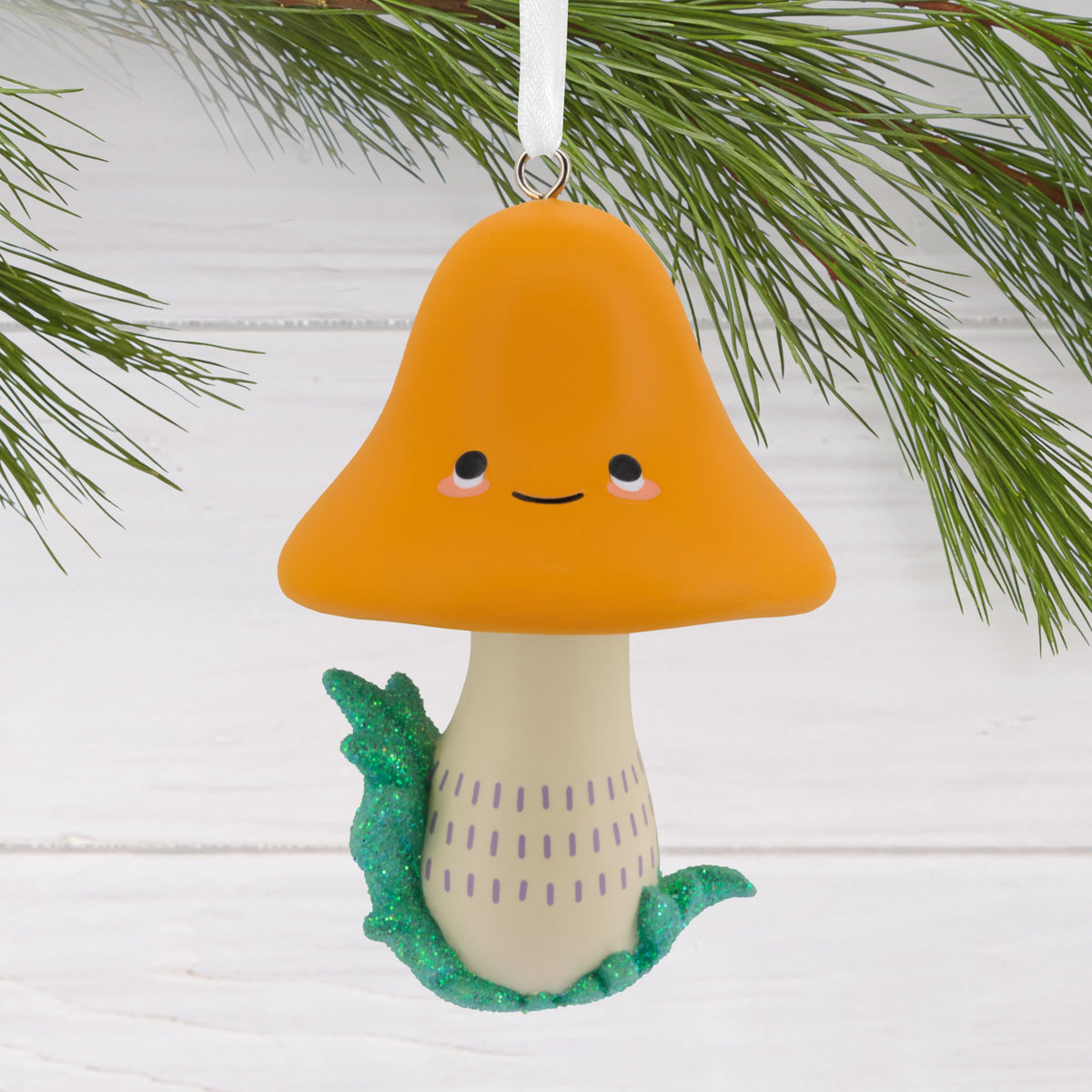 Orange-capped smiling mushroom ornament hanging from a pine branch