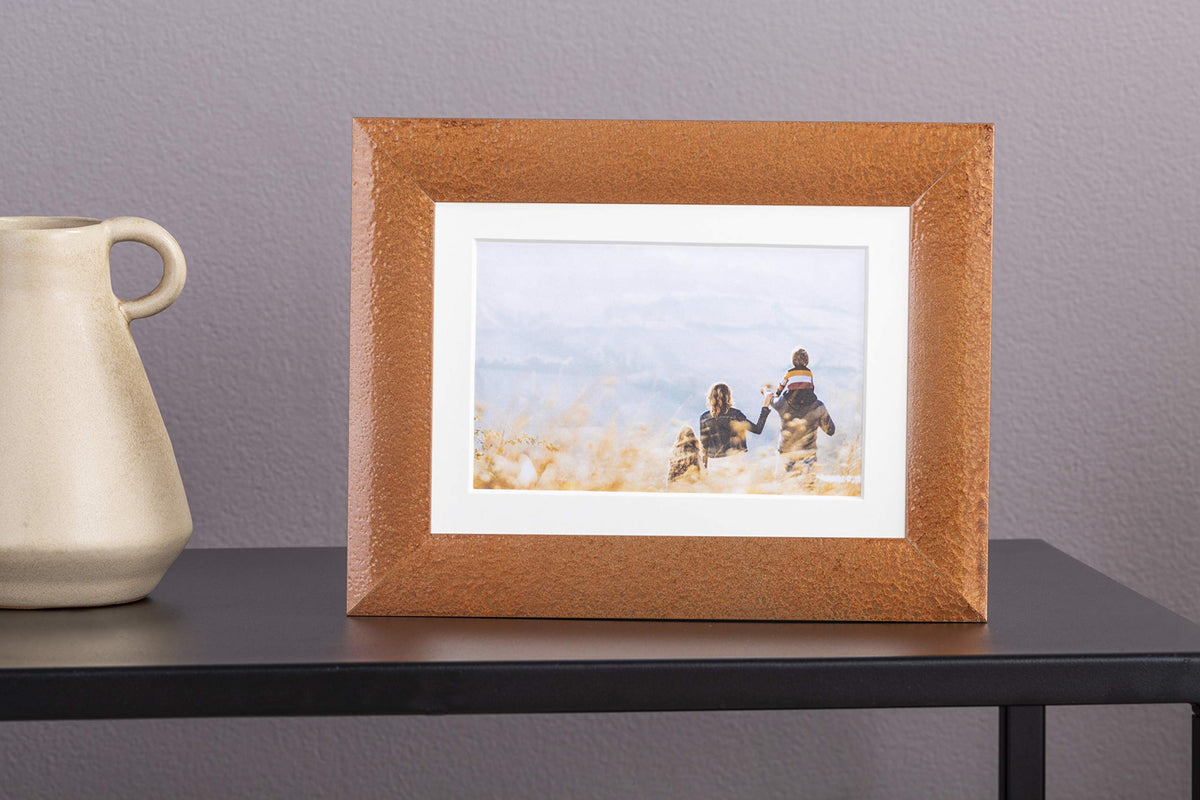 Copper hammered picture frame on a black side table next to a cream vase