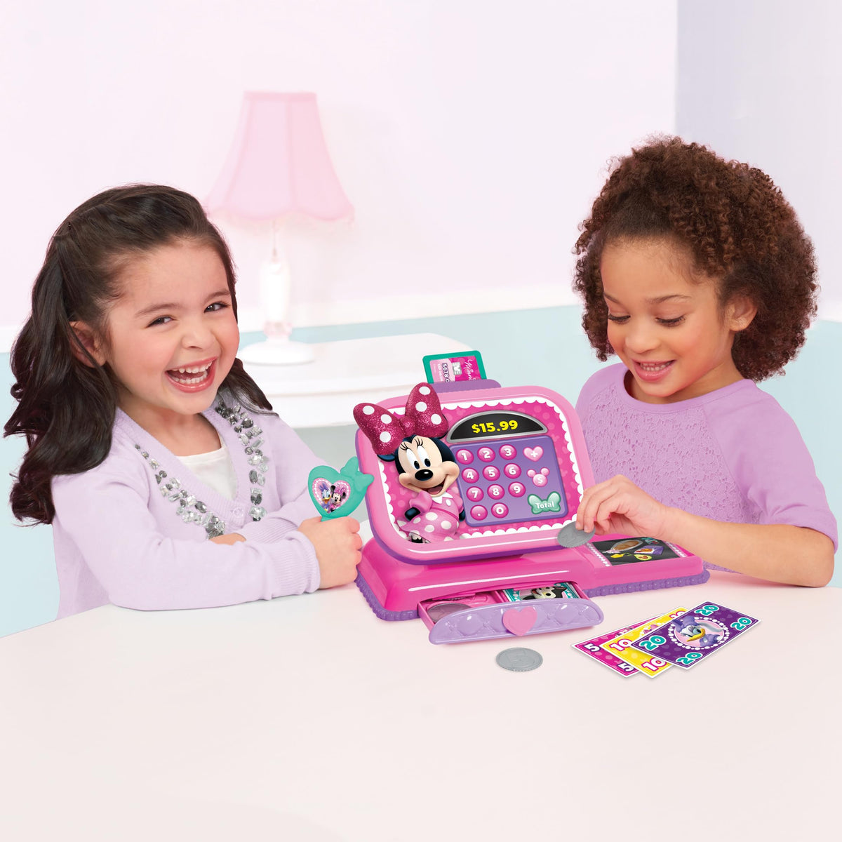 Two girls laughing while playing shop with the pink Minnie Mouse toy cash register and play money