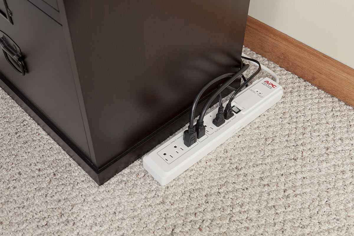 White surge protector on carpet beside a dark wood cabinet with four plugs in use