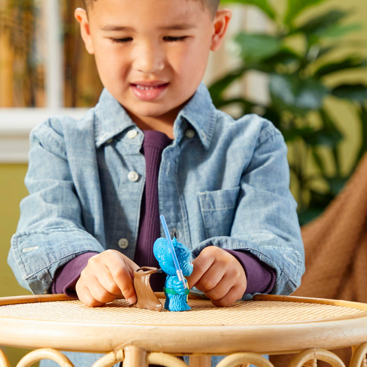 Boy fitting the brown cape onto the blue furry figure on a rattan table