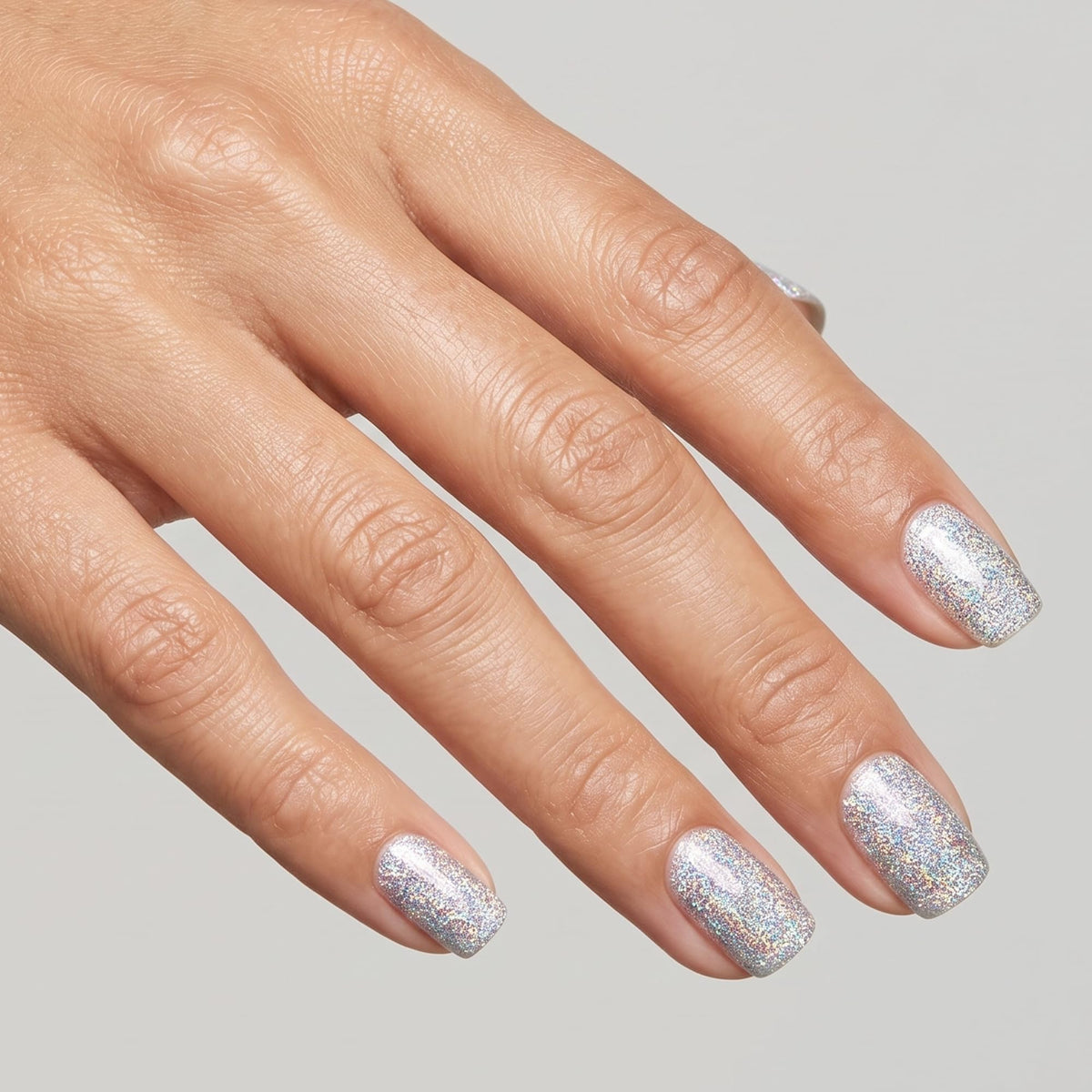 Hand with short square nails painted in silver holographic glitter