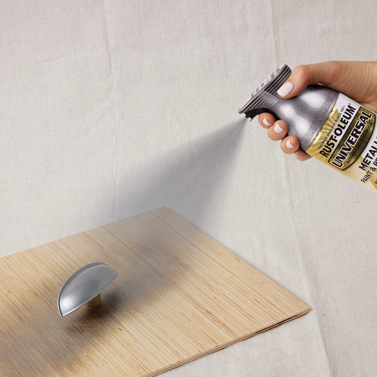 Hand spraying metallic grey paint onto a cabinet cup pull on a wood board