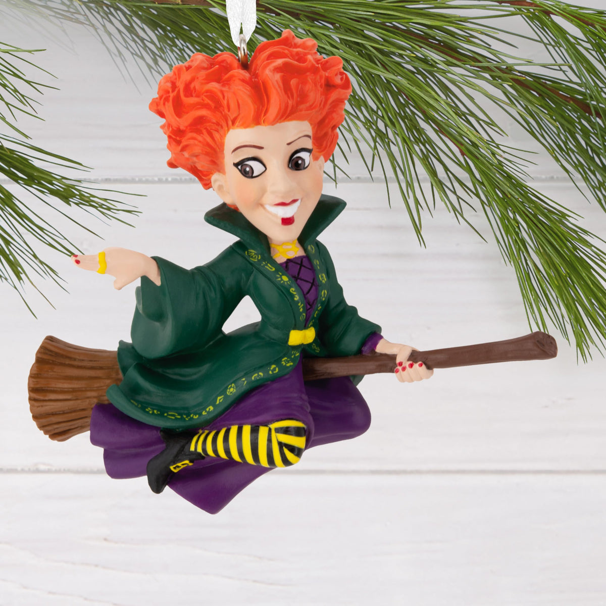 Witch on a broomstick ornament hanging from a pine branch