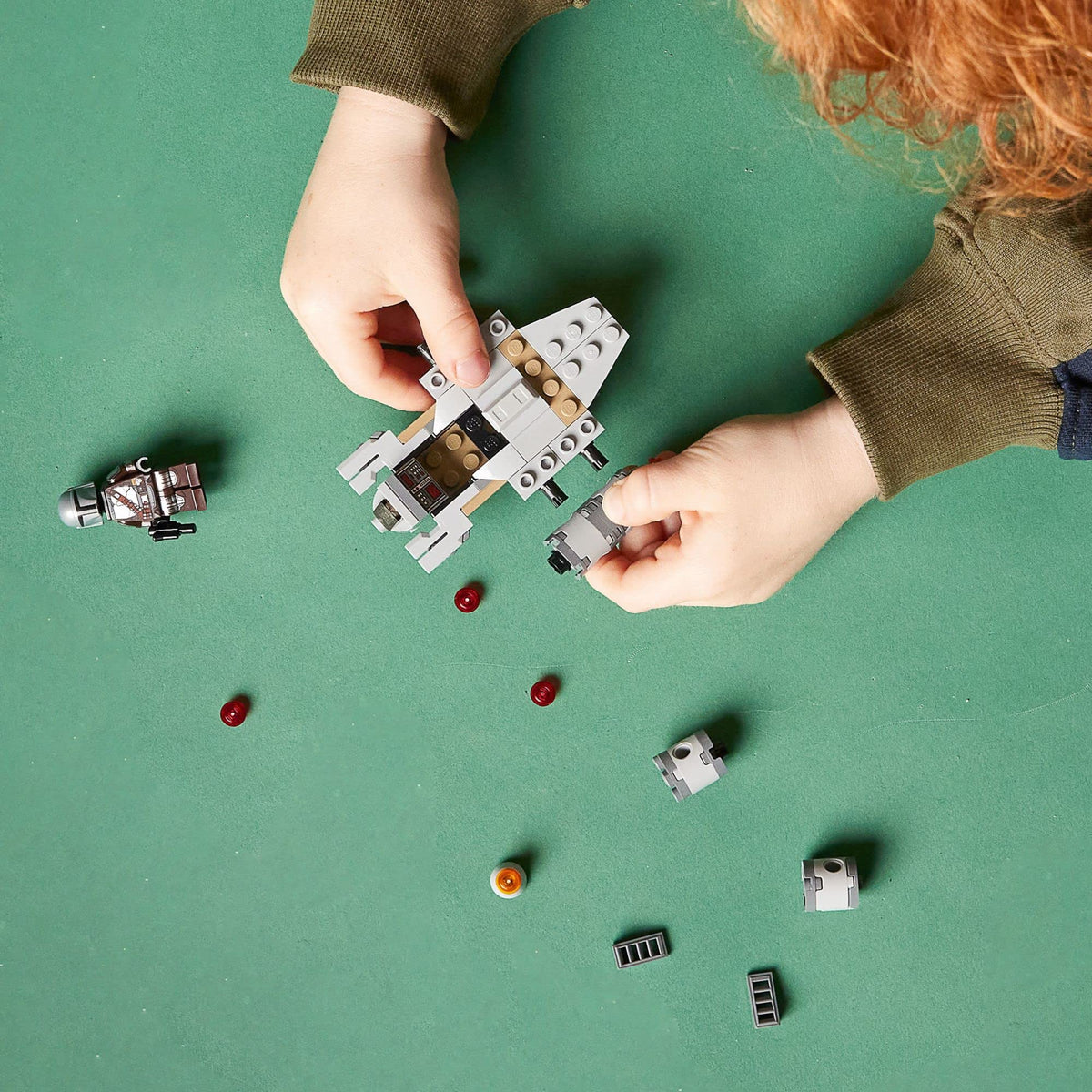 Child's hands building the Razor Crest on a green table with loose bricks and minifigure