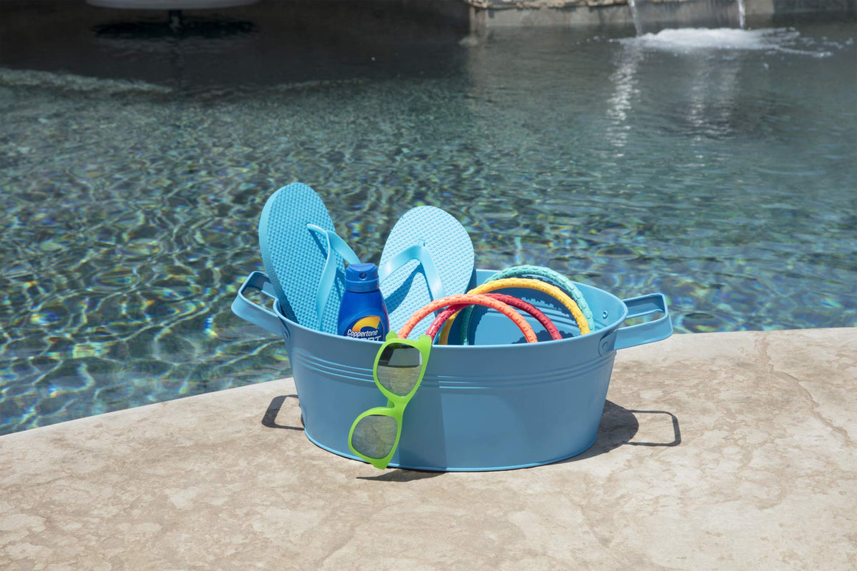 Light blue painted metal tub with flip-flops, sunscreen and pool rings by a pool