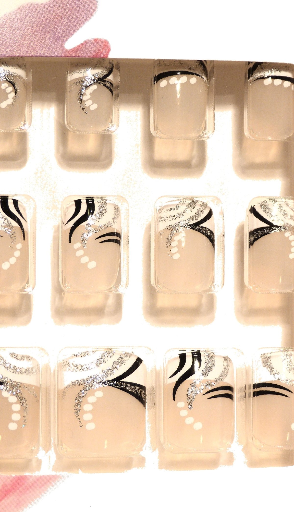 Close-up of clear-tip false nails decorated with black stripes, glitter and white dots