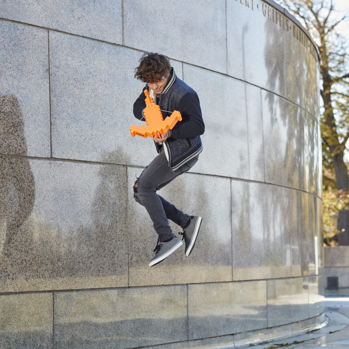 Teen jumping in the air holding the orange blocky crossbow beside a curved wall
