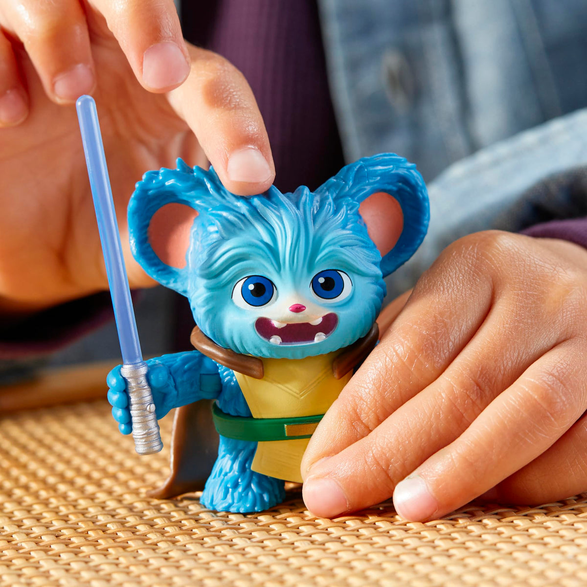 Child patting the blue creature figure's head as it holds a blue lightsaber