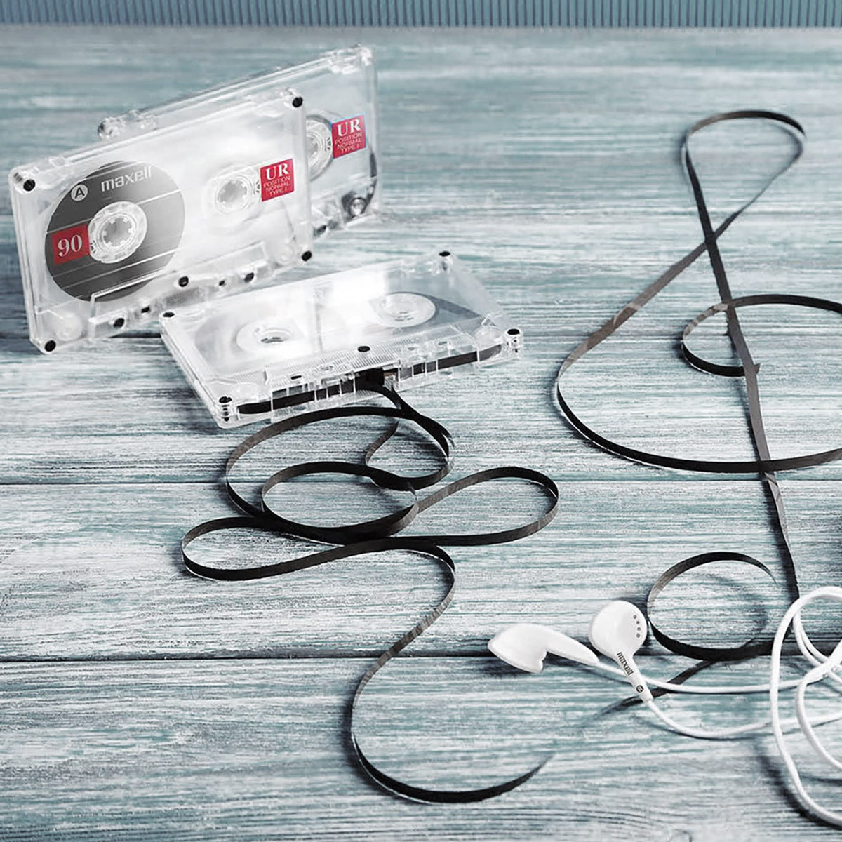 Clear audio cassettes on a wooden table with loose tape and white earbuds