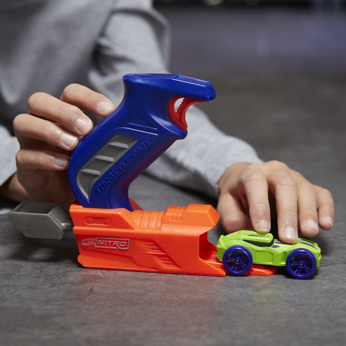 Hand loading the green foam car into the orange base of the blue-handled launcher