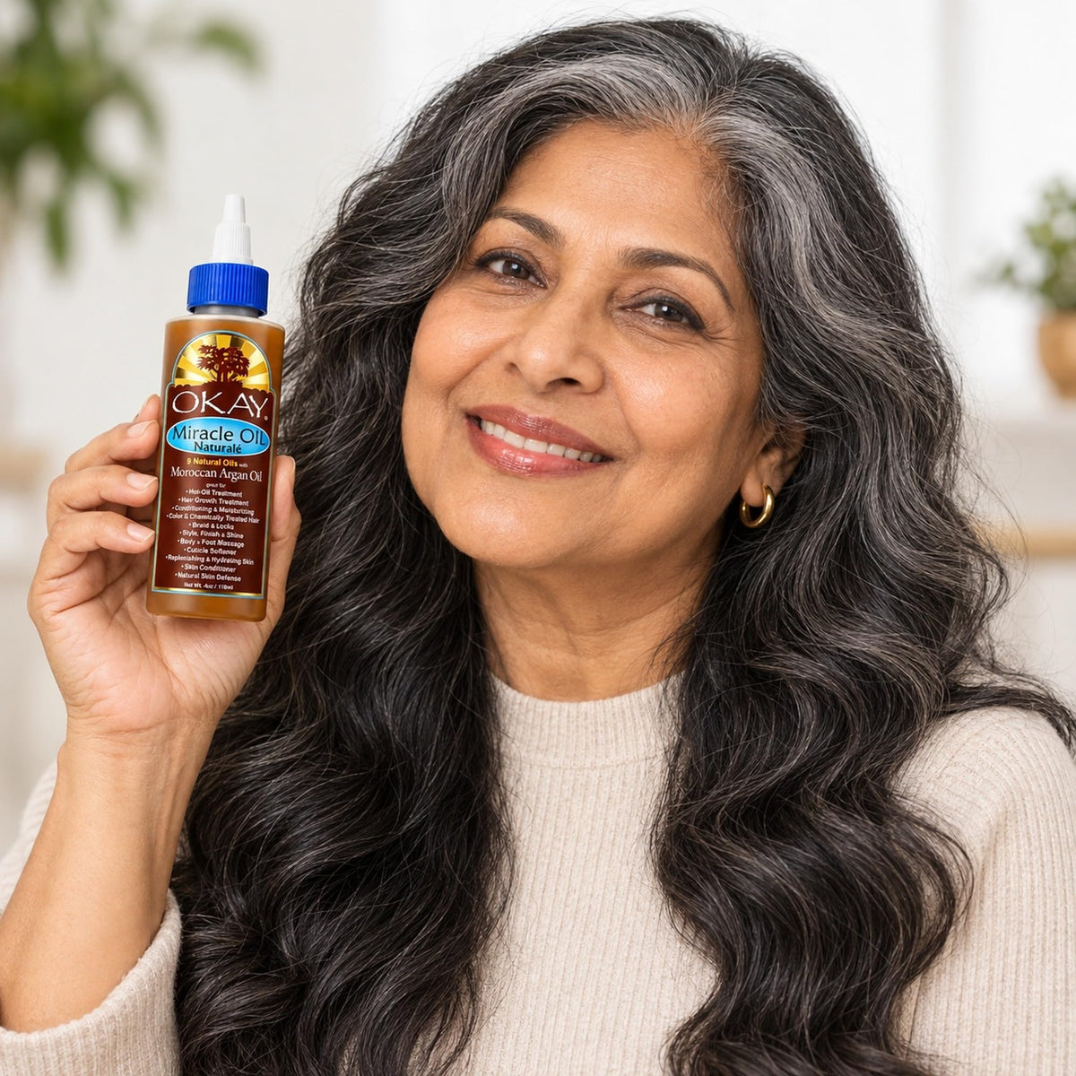 Woman with long grey-streaked wavy hair holding up the Miracle Oil bottle