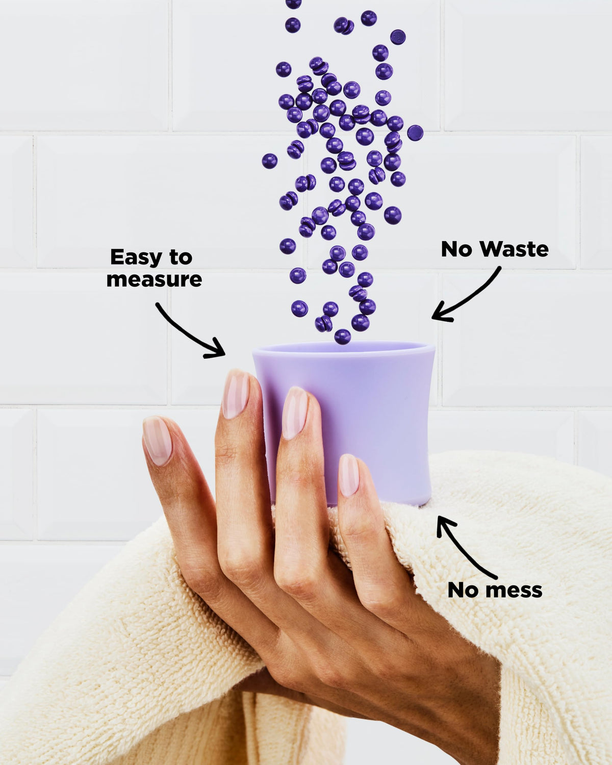 Purple wax beads pouring into a lilac silicone measuring cup held in a hand, labelled easy to measure, no waste, no mess