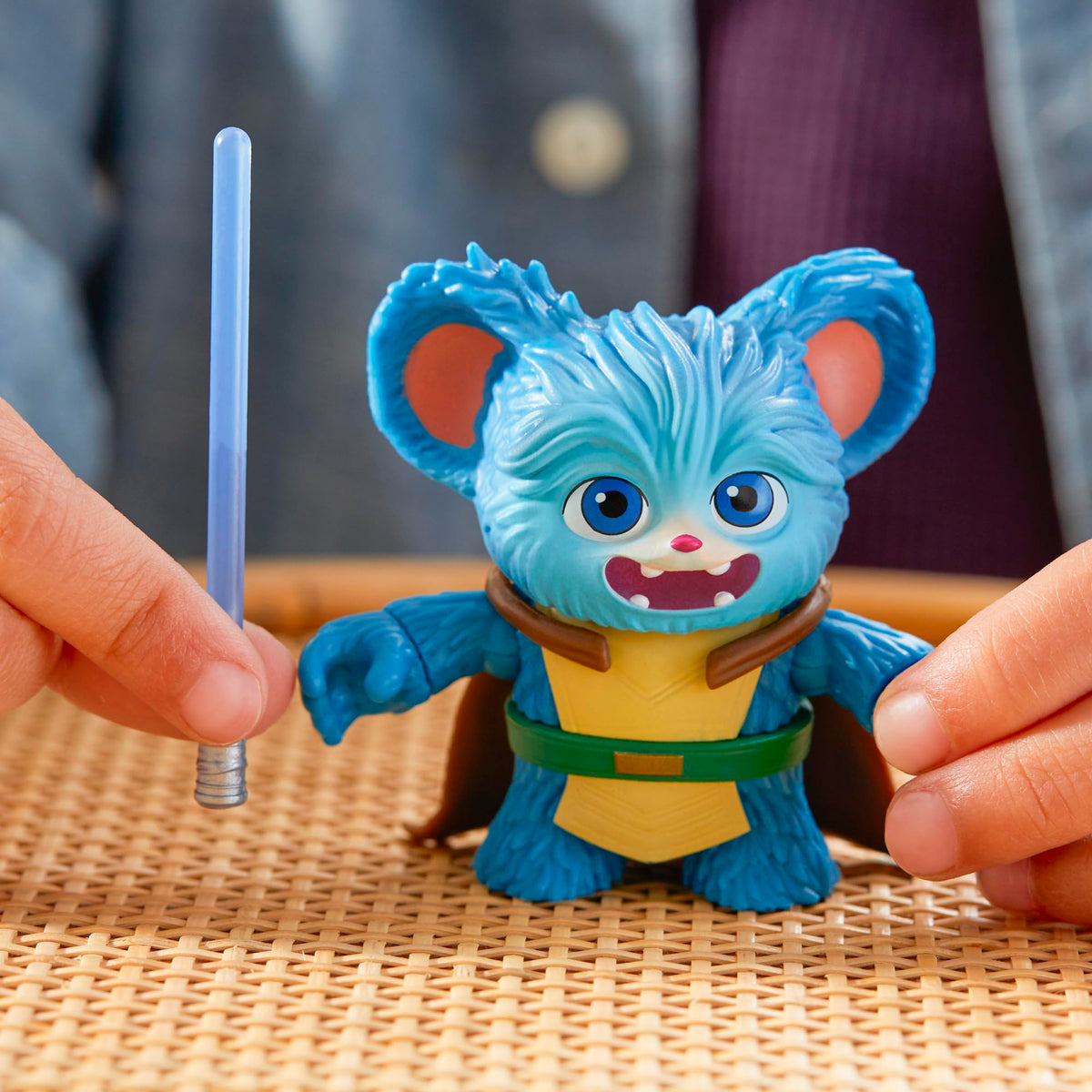Blue furry figure in a cream tunic and green belt beside a held lightsaber