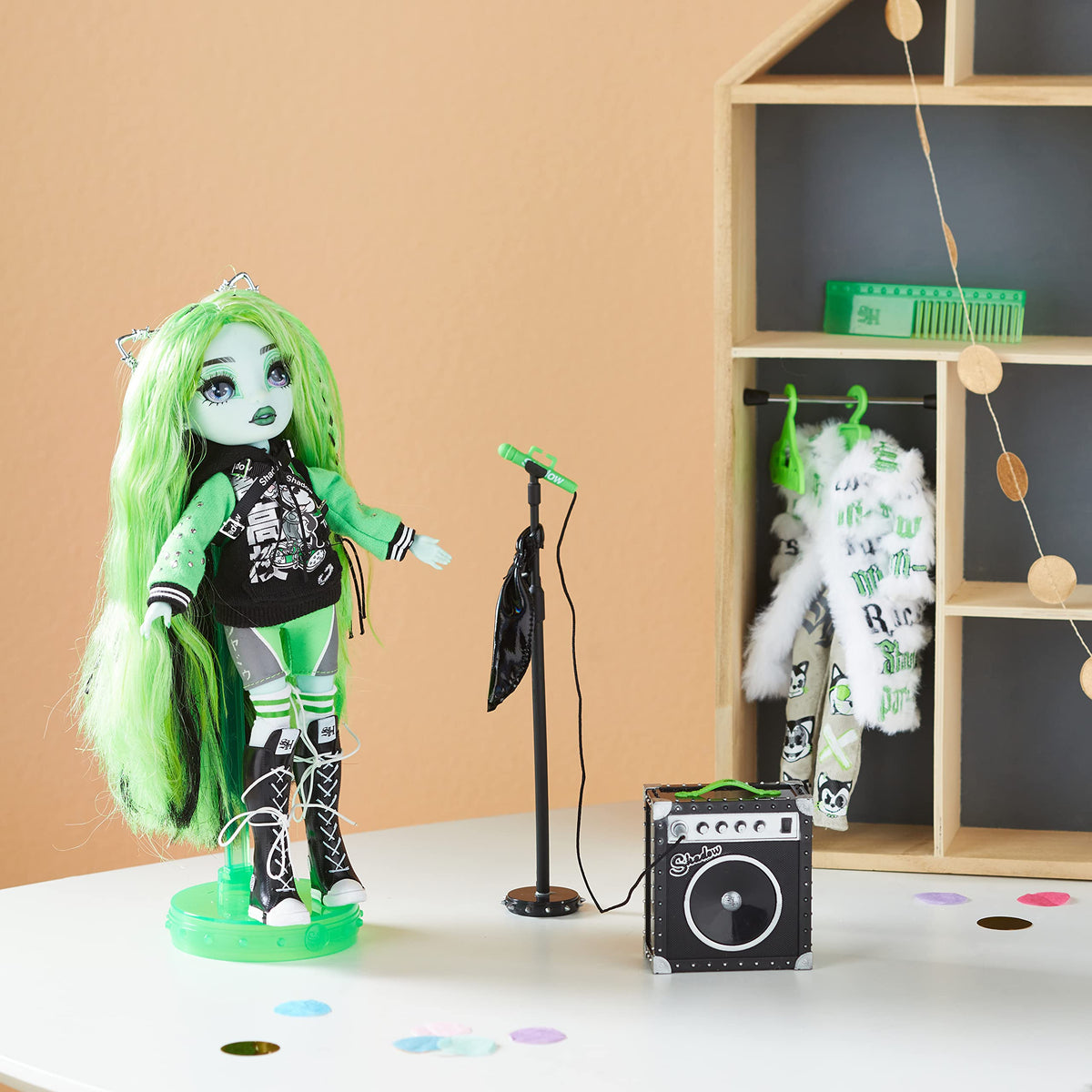 Green-haired doll on a stand beside a microphone, amp and a fur coat on a hanger