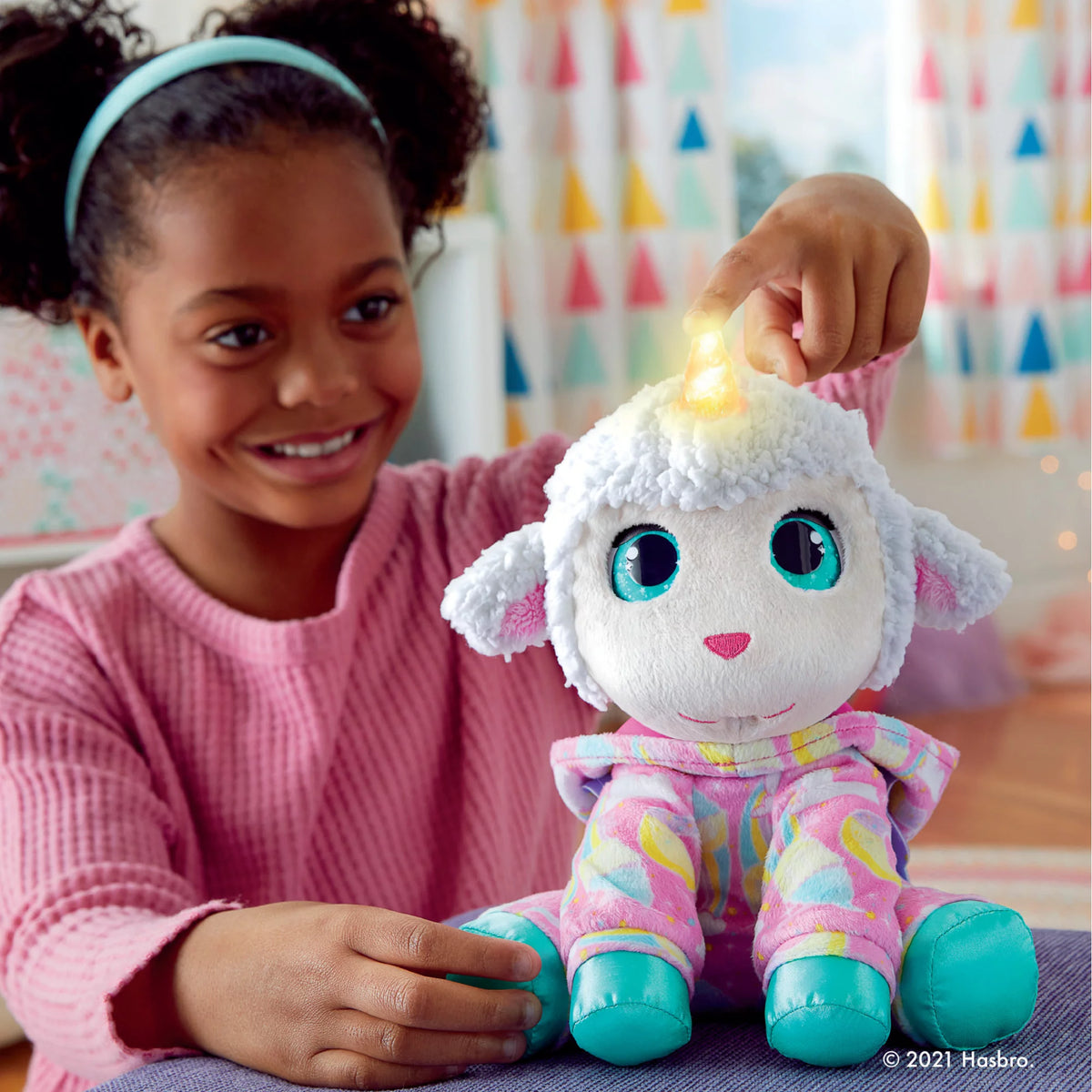 Girl pressing the glowing horn of the white lamb plush in pink pajamas